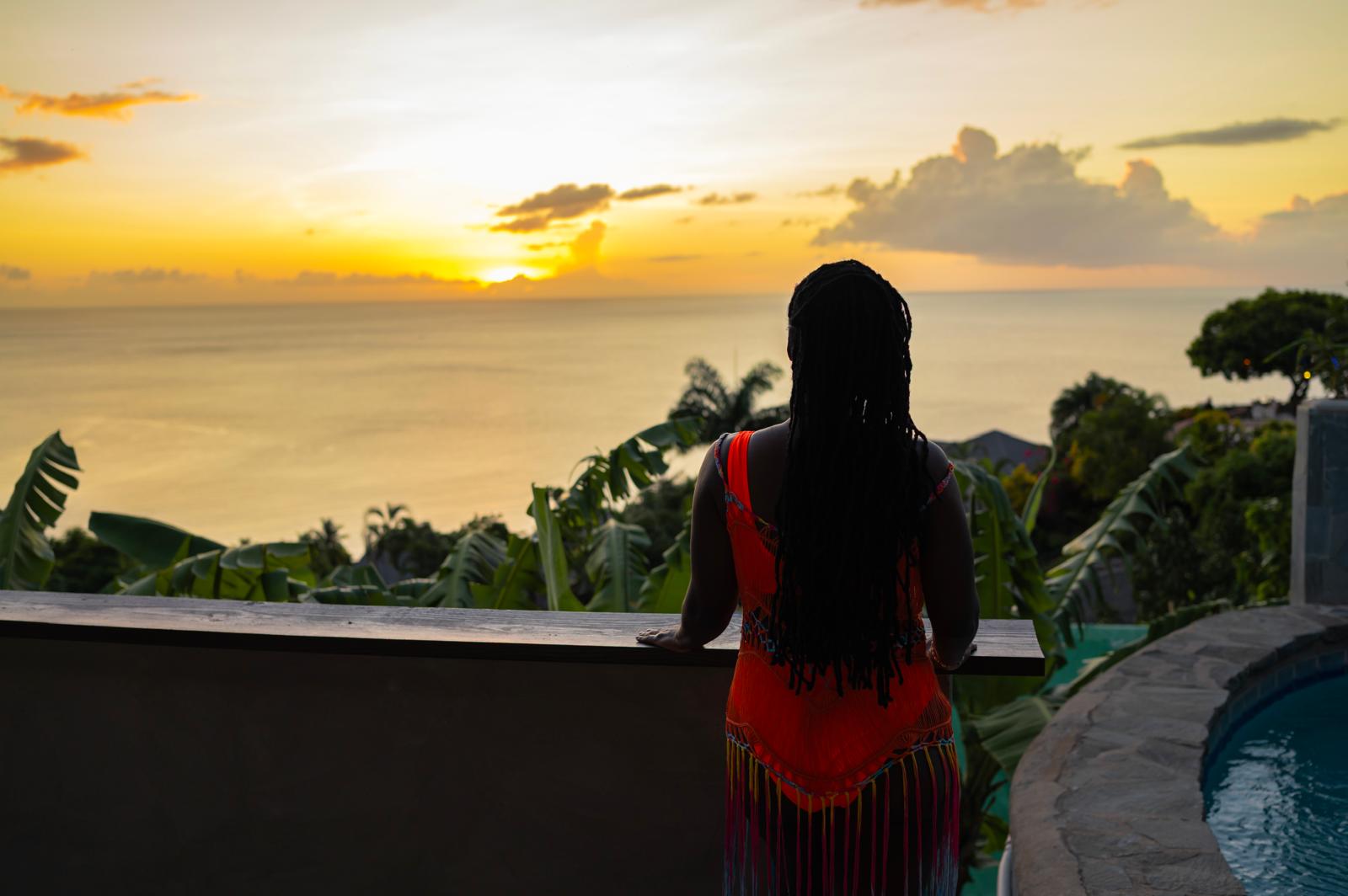 A Black woman standing at a railing watching the sun rise over the ocean